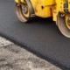 Roller flattening new asphalt pavement